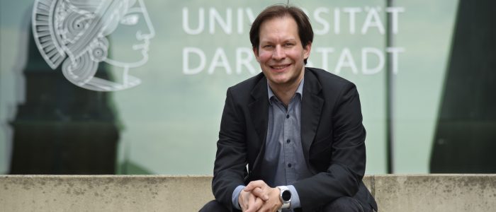 Der neue Professor Björn Scheuermann sitzt auf der Treppe vor der TU Darmstadt
