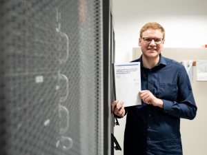 Marvin Härdtlein steht in einem Serverraum und zeigt seine Masterarbeit mit dem Titel ""Hybrid Switch: Dynamic Flow Rule Offloading on High Performance Networking Hardware"